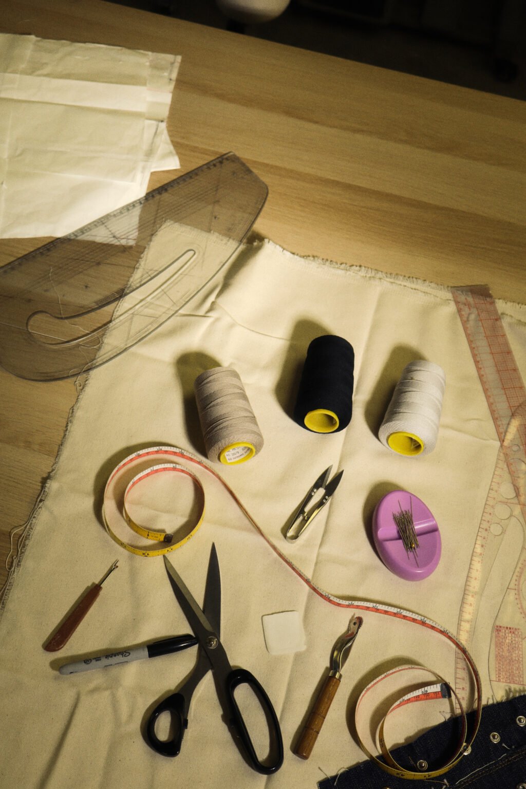 Sewing tools laid out on calico: thread cones, scissors, a measuring tape, pins and pattern rulers