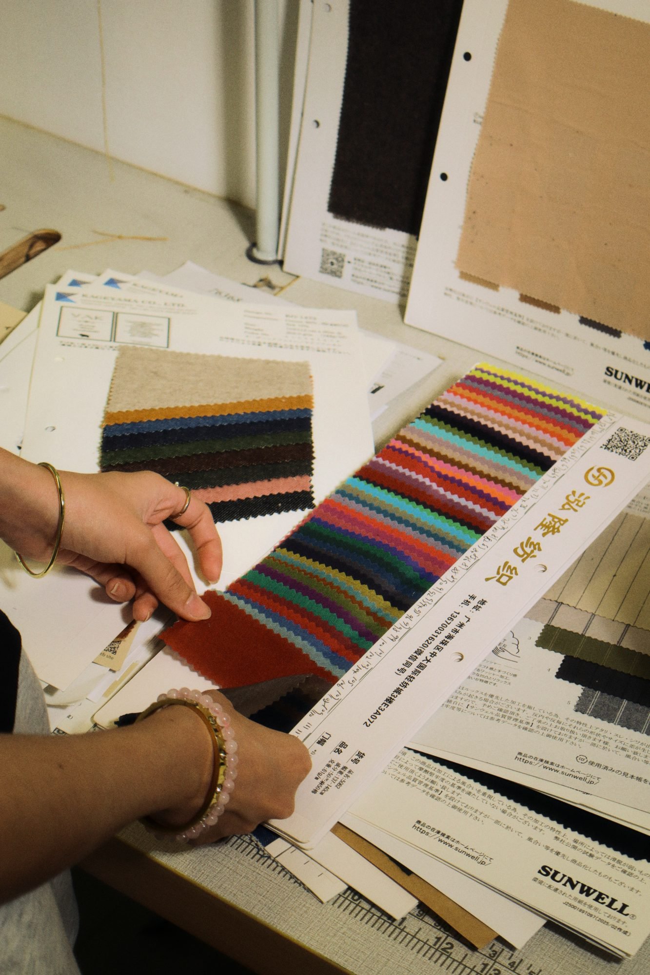Hands holding a fabric swatch card of coloured knits